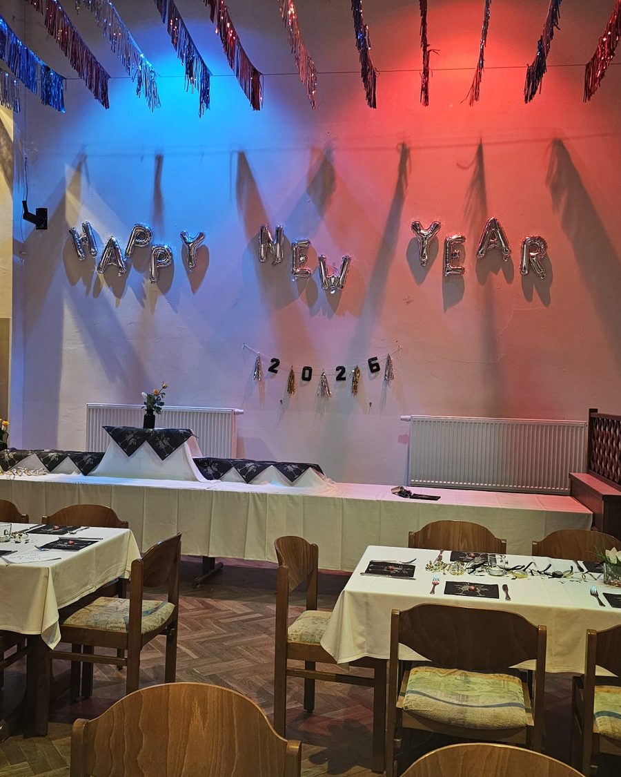 Der große Saal mit „Happy New Year“-Schriftzug, farbigem Licht und eingedeckten Tischen